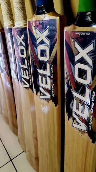 Row of hand-crafted Velox English Willow cricket bats with orange lightning bolt branding